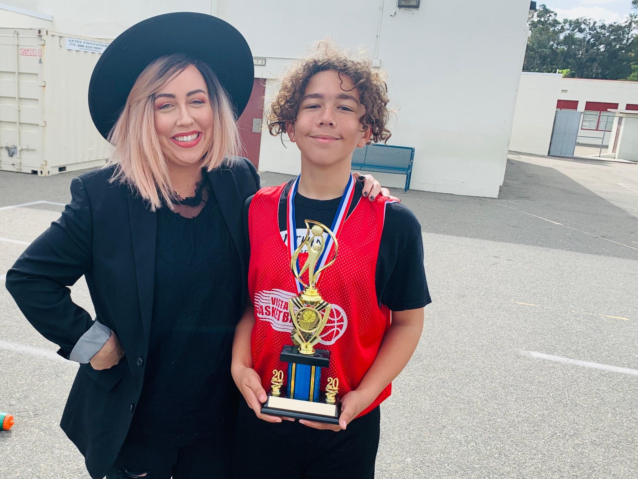 Heather with her son, who is holding a youth basketball trophy in a red Vista Basketball jersey, early in her photography journey.